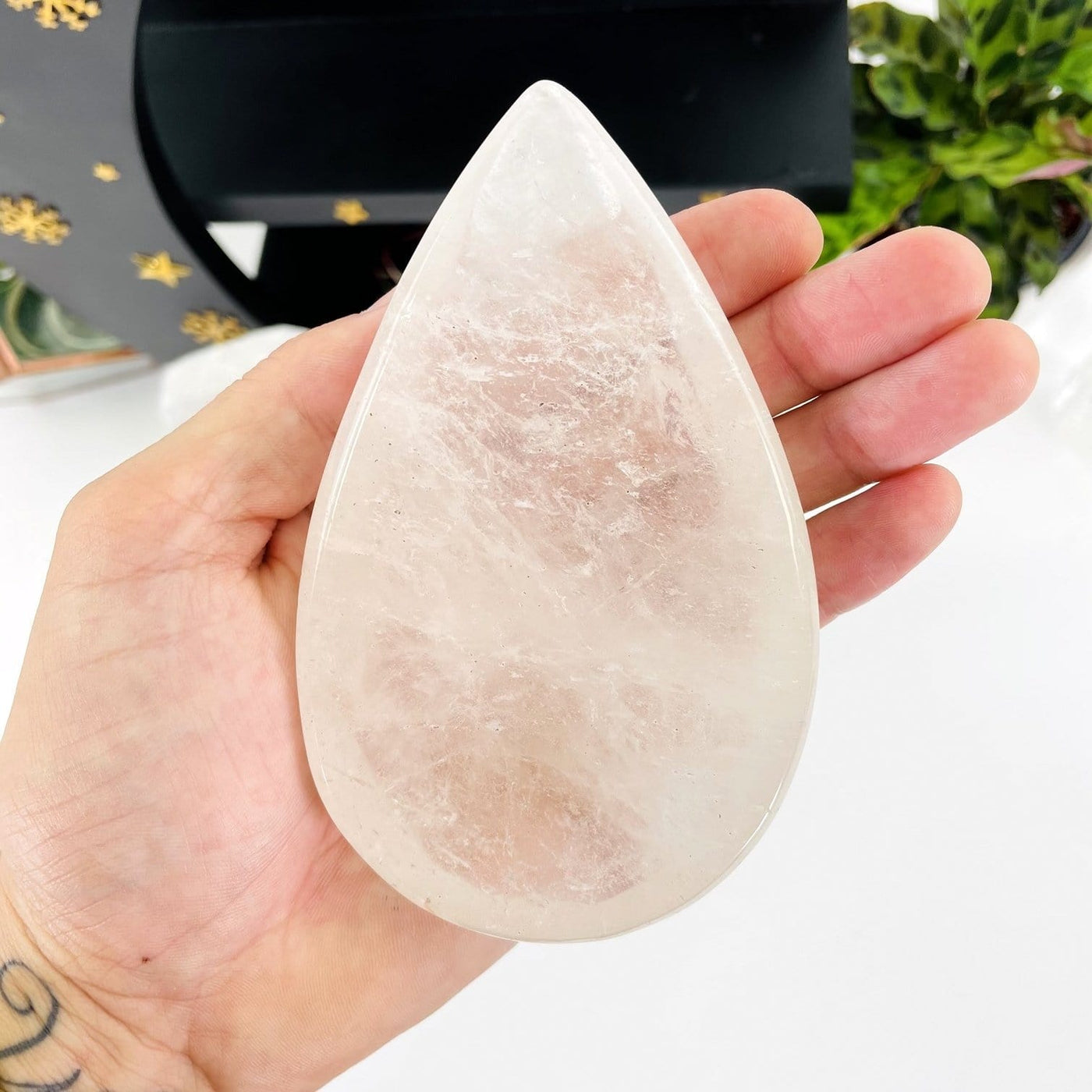 hand holding up Clear Quartz Tear Drop Shape with decorations in the background