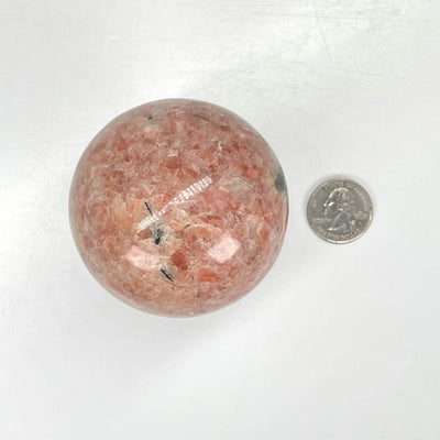 overhead view of sunstone polished sphere with quarter for size reference