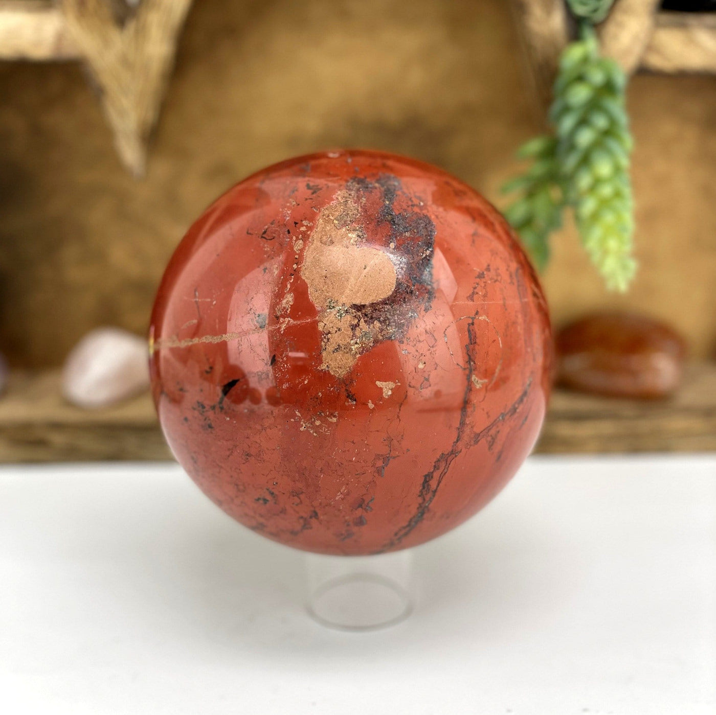 Red Jasper Polished Sphere on a stand in front of wooden display