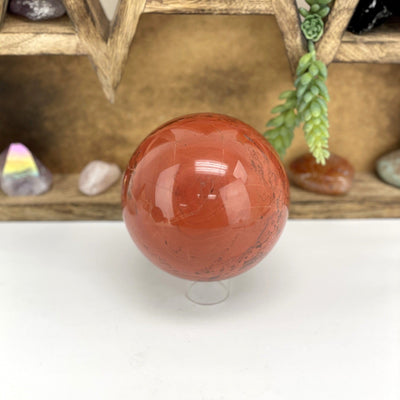 Red Jasper Polished Sphere on stand in front of wooden display with crystals