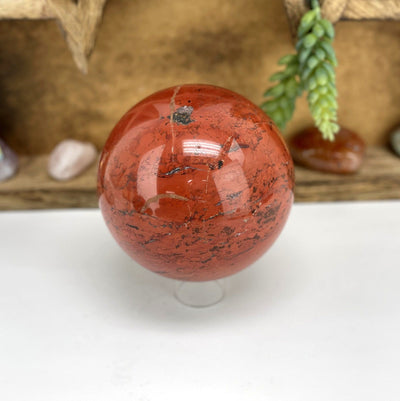 Red Jasper Polished Sphere in front of wooden display with crystals