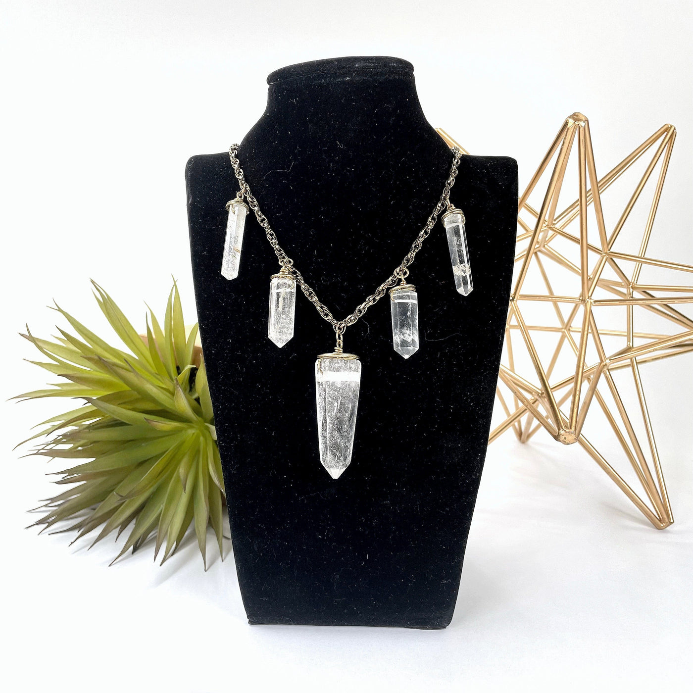 crystal quartz point five pendant necklace on bust display in front of backdrop