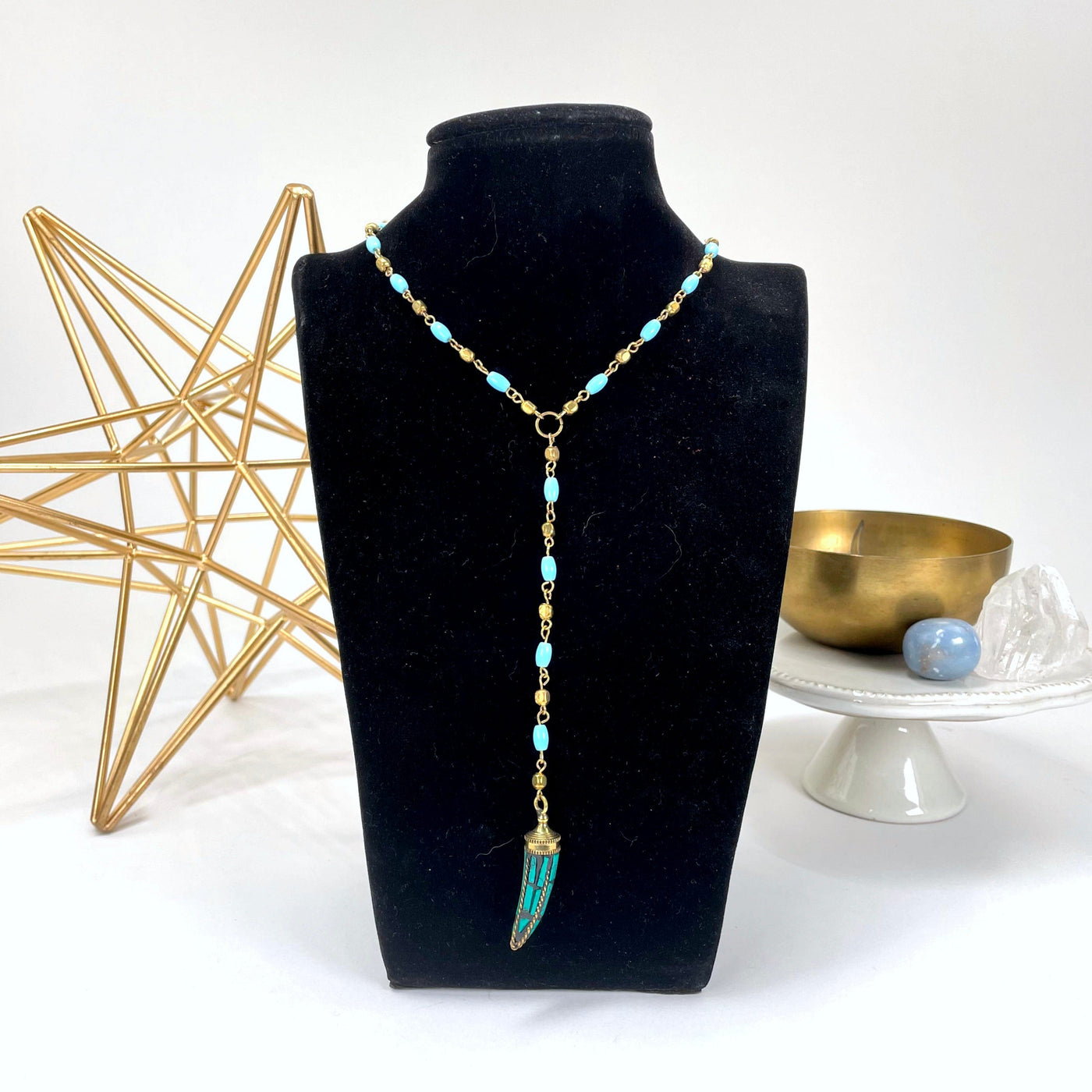 tibetan style beaded necklace with turquoise horn pendant on bust display in front of backdrop
