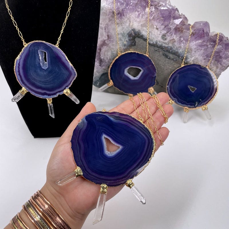 large purple agate slices with crystal quartz point necklaces displayed to show the differences in the agate 