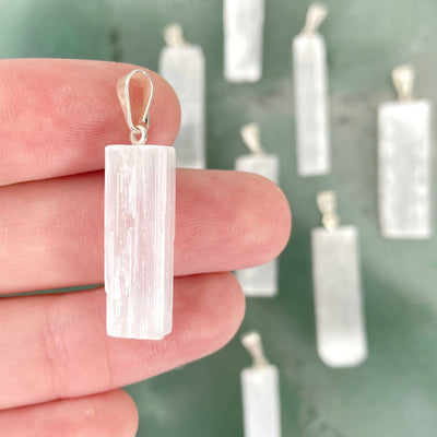 close up of selenite rough pendant in hand with others in background