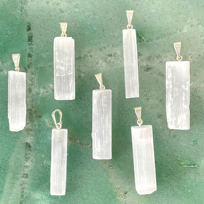 many selenite rough pendants on green background for possible variations 