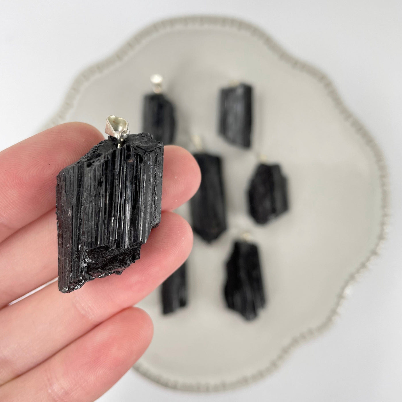 close up of black tourmaline rough pendant in hand for size reference with others in background