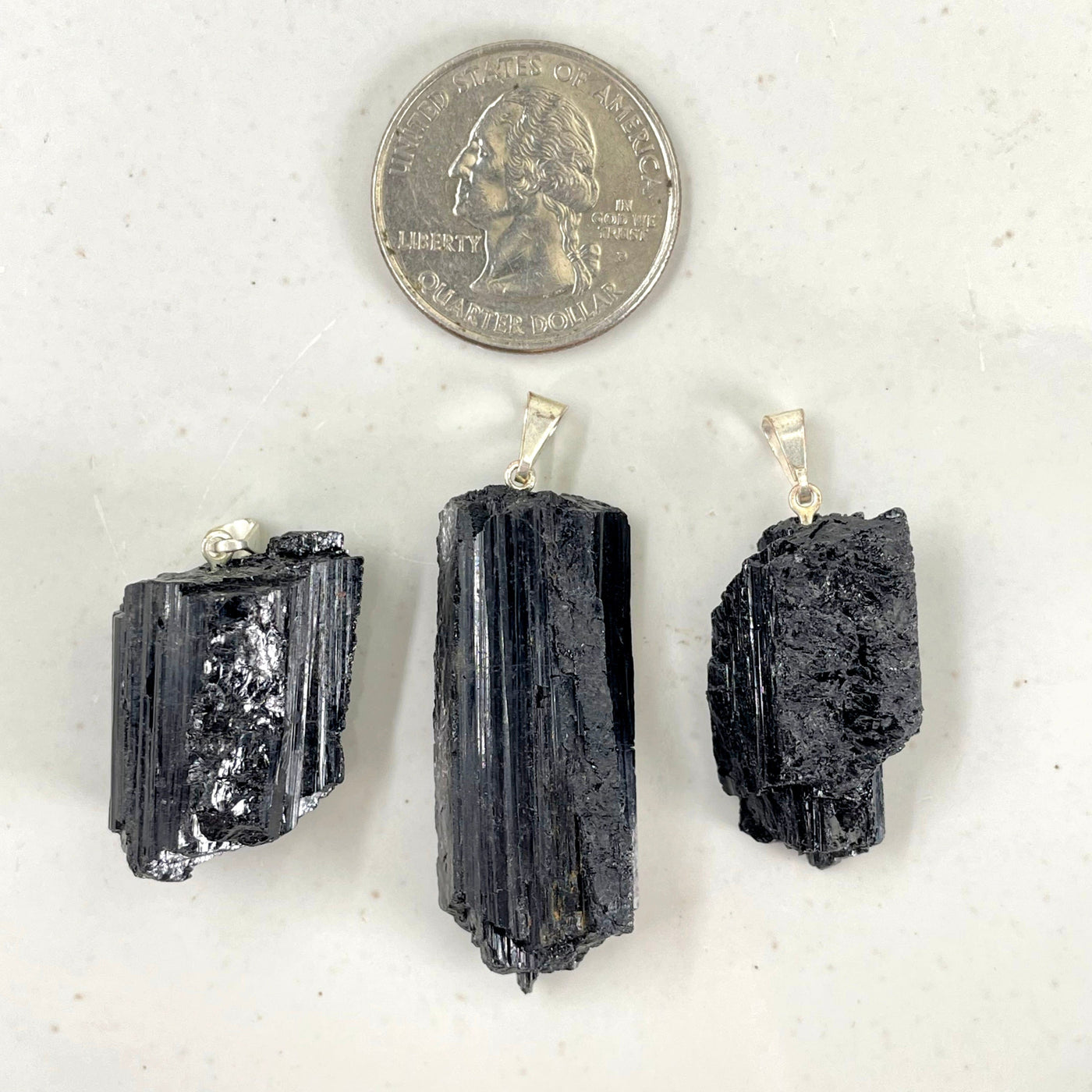 three black tourmaline rough pendants with quarter for size reference