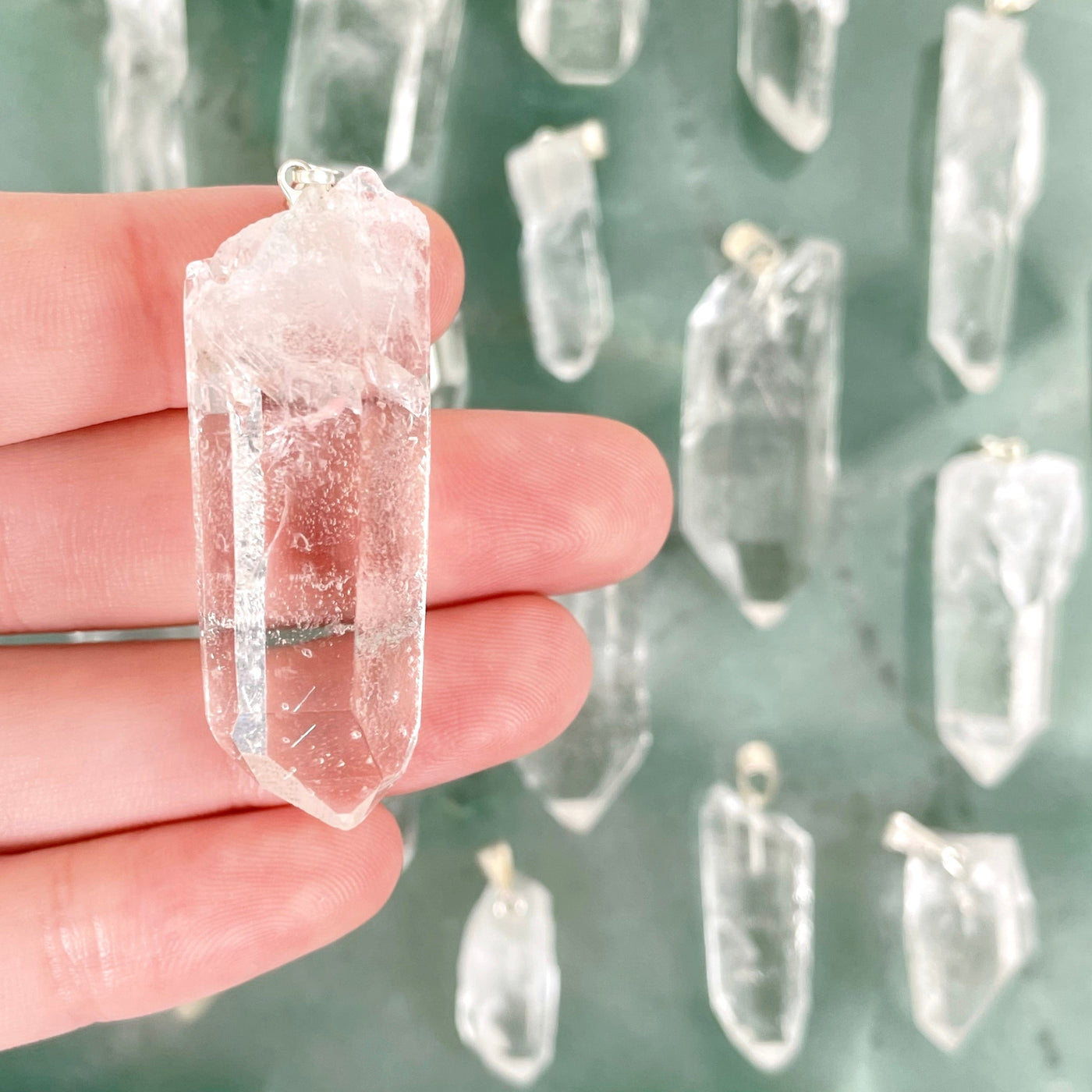 close up of crystal quartz rough point pendant in hand for size reference with others in background