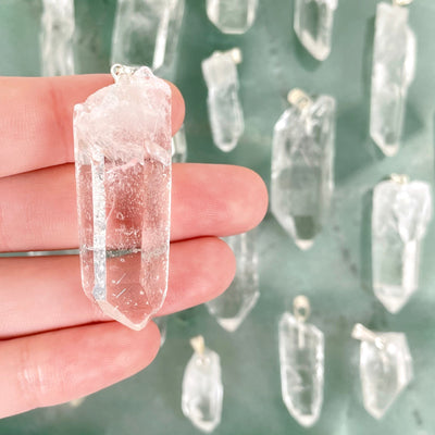 close up of crystal quartz rough point pendant in hand for size reference with others in background