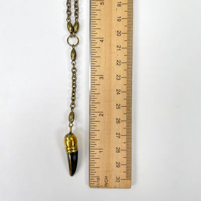 close up of gold and black horn pendant with ruler for size reference