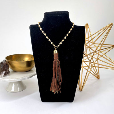 tibetan style beaded necklace with tassel pendant on bust display in front of backdrop
