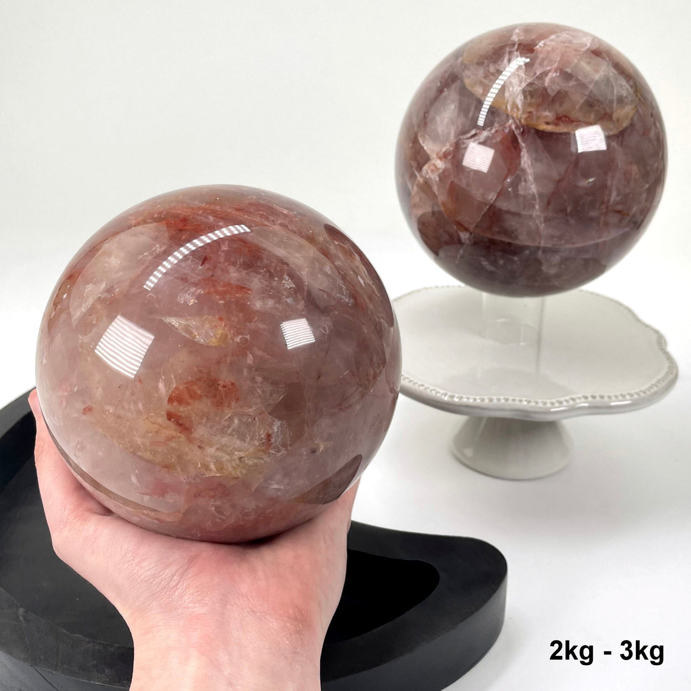 one 2kg - 3kg guava polished sphere in hand for size reference with one other in background display