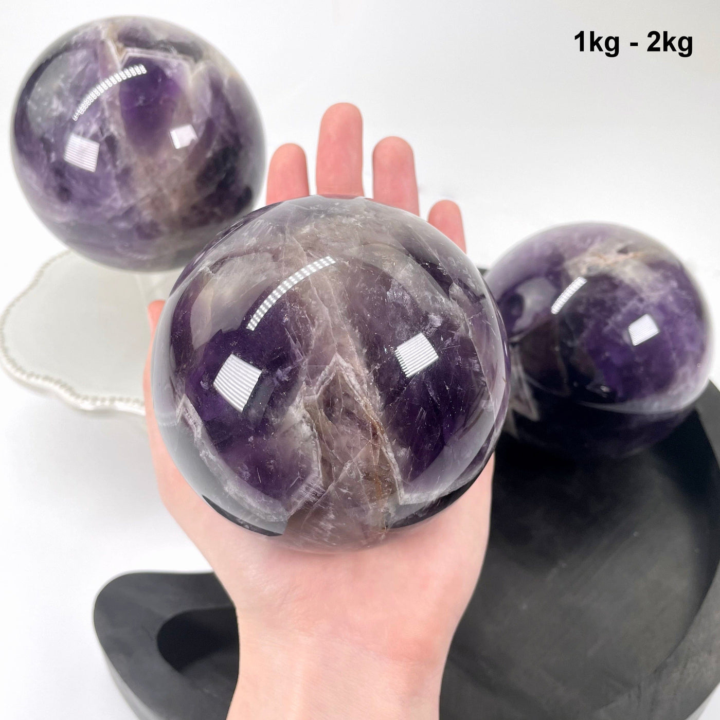 1kg - 2kg chevron amethyst polished sphere in hand with two others in background display