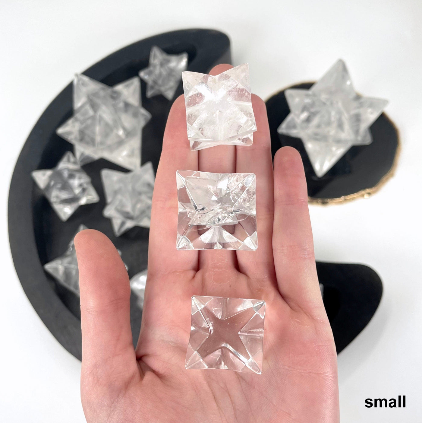 three small crystal quartz merkabah stars in hand for size reference and possible variations with others in background display