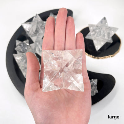 one large crystal quartz merkabah star in hand for size reference with others in background display