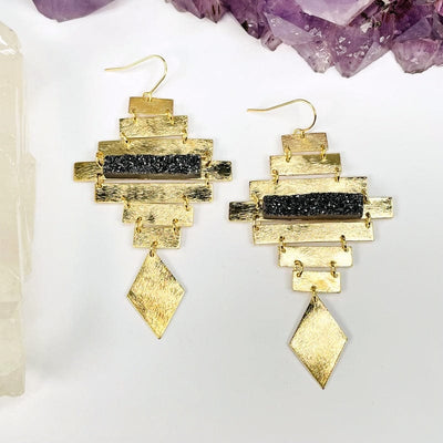 gold earrings with a diamond shape at the bottom with a black diamond druzy bar that accents the center 