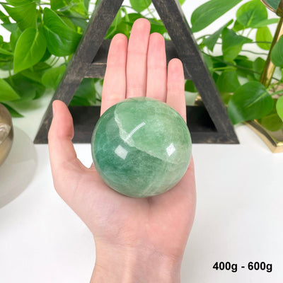 one 400g - 600g green fluorite sphere in hand for size reference
