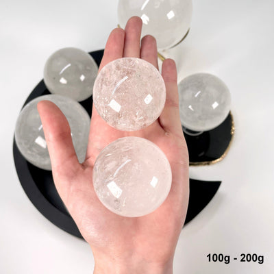 two 100g - 200g crystal quartz polished spheres in hand for size reference and possible variations