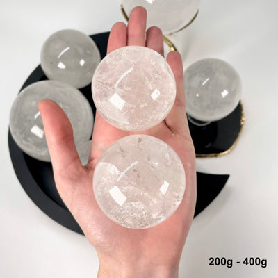 two 200g - 400g crystal quartz polished spheres in hand for size reference and possible variations