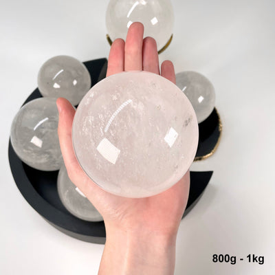 one 800g - 1kg crystal quartz polished sphere in hand for size reference