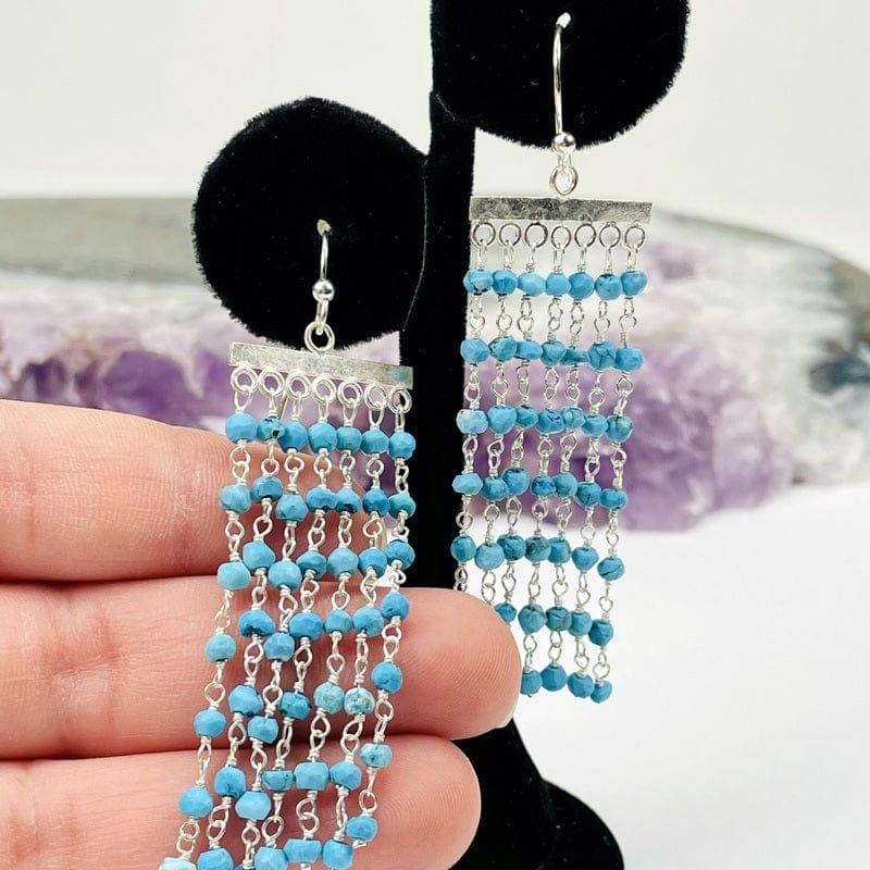 hand holding gemstone cascade earrings with crystals in the background