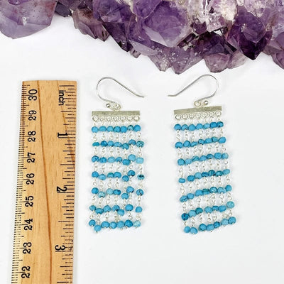 gemstone cascade earrings next to a ruler for size reference on white background
