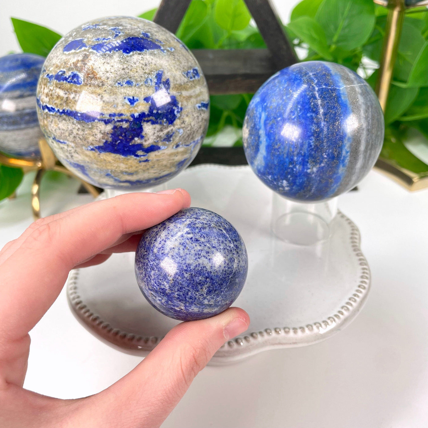 three different lapis lazuli polished sphere weights on display with hand on one 