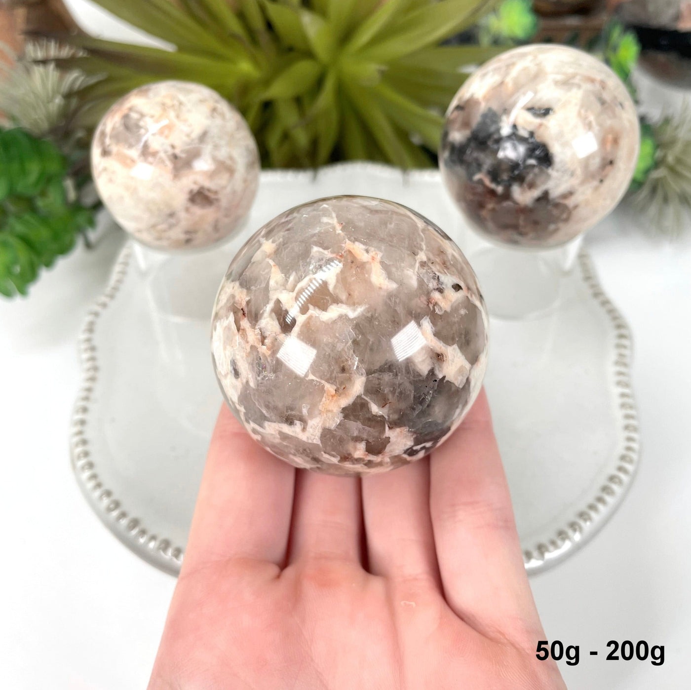 one 50g - 200g sphere in hand for size reference with two others in background display