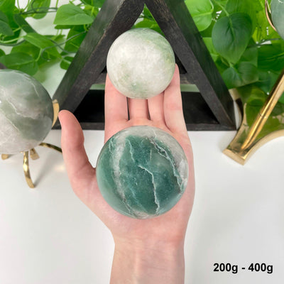 two 200g - 400g green and white quartz spheres in hand for size reference and possible variations