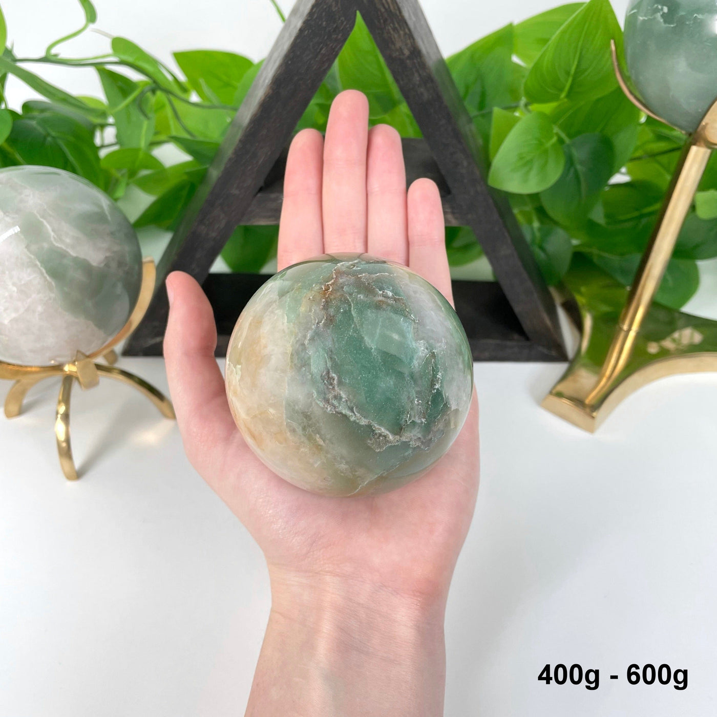 one 400g - 600g green and white quartz sphere in hand for size reference