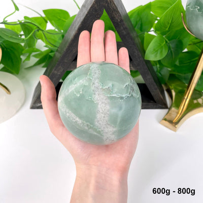 one 600g - 800g green and white quartz sphere in hand for size reference