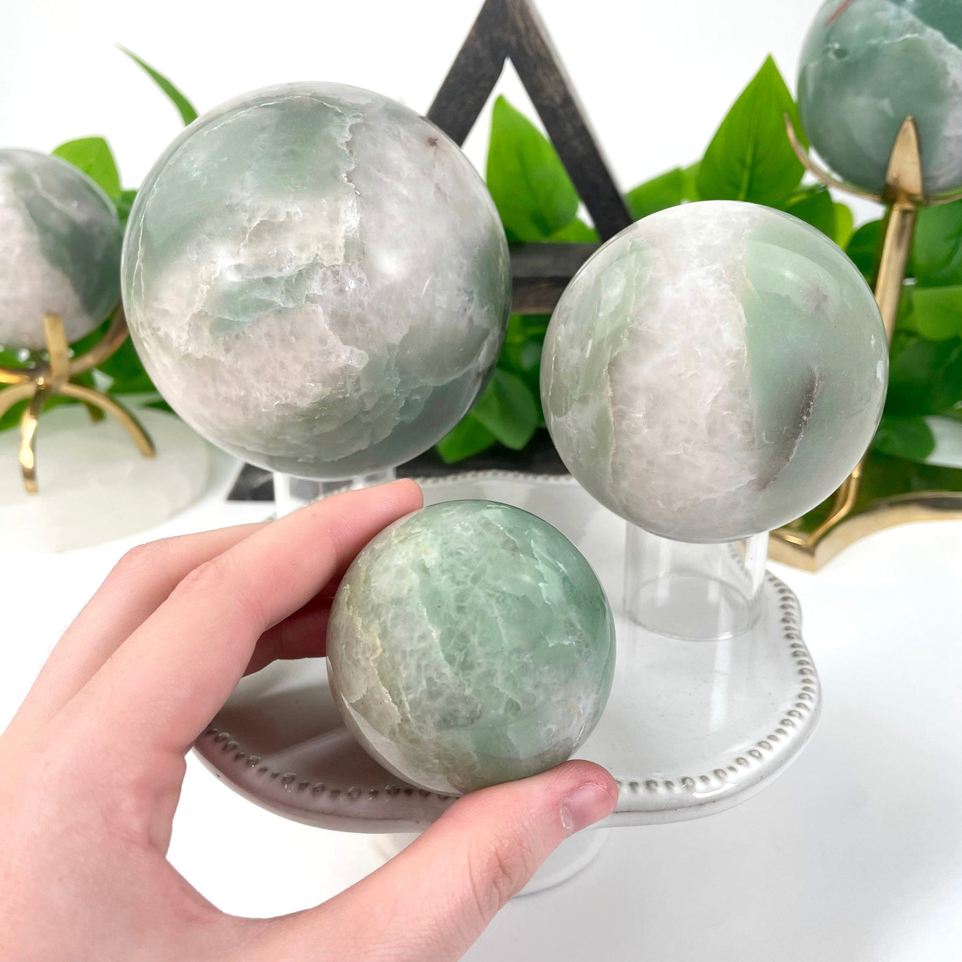 three different green and white quartz sphere weights on display for size comparison with one in hand for size reference