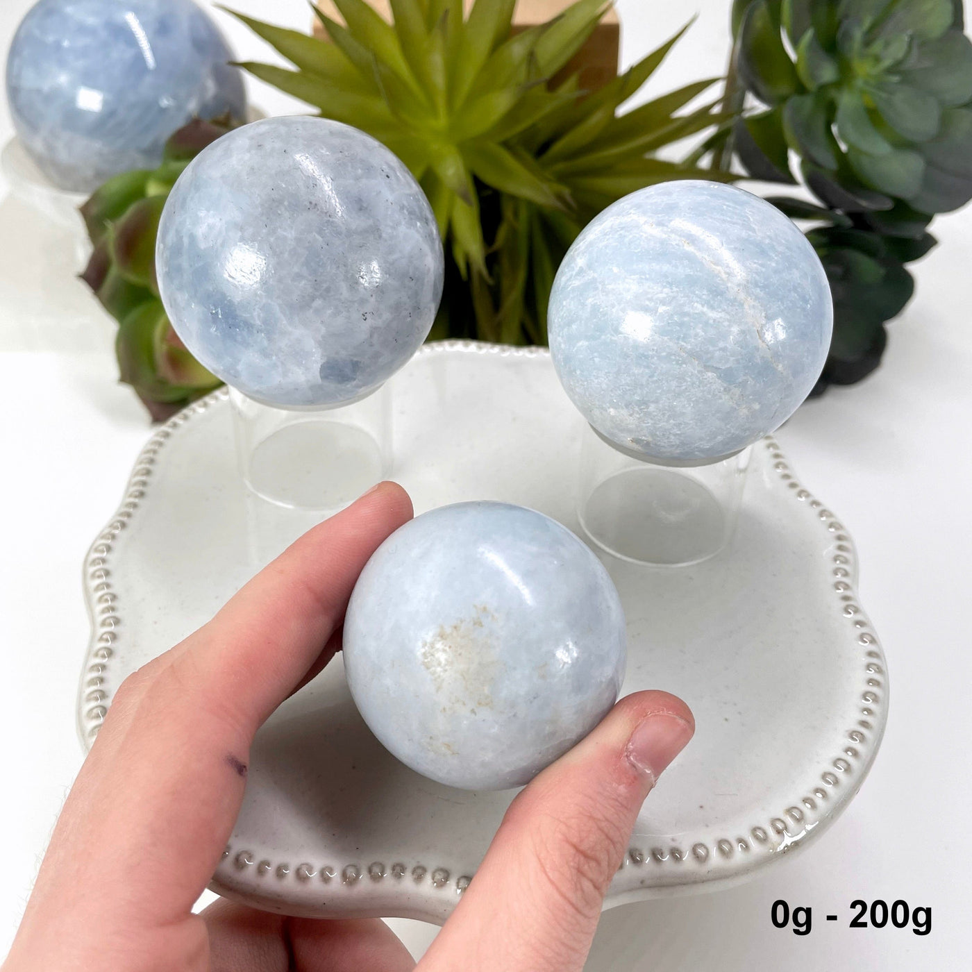 three 0g - 200g blue calcite spheres on display for possible variations with one in hand for size reference
