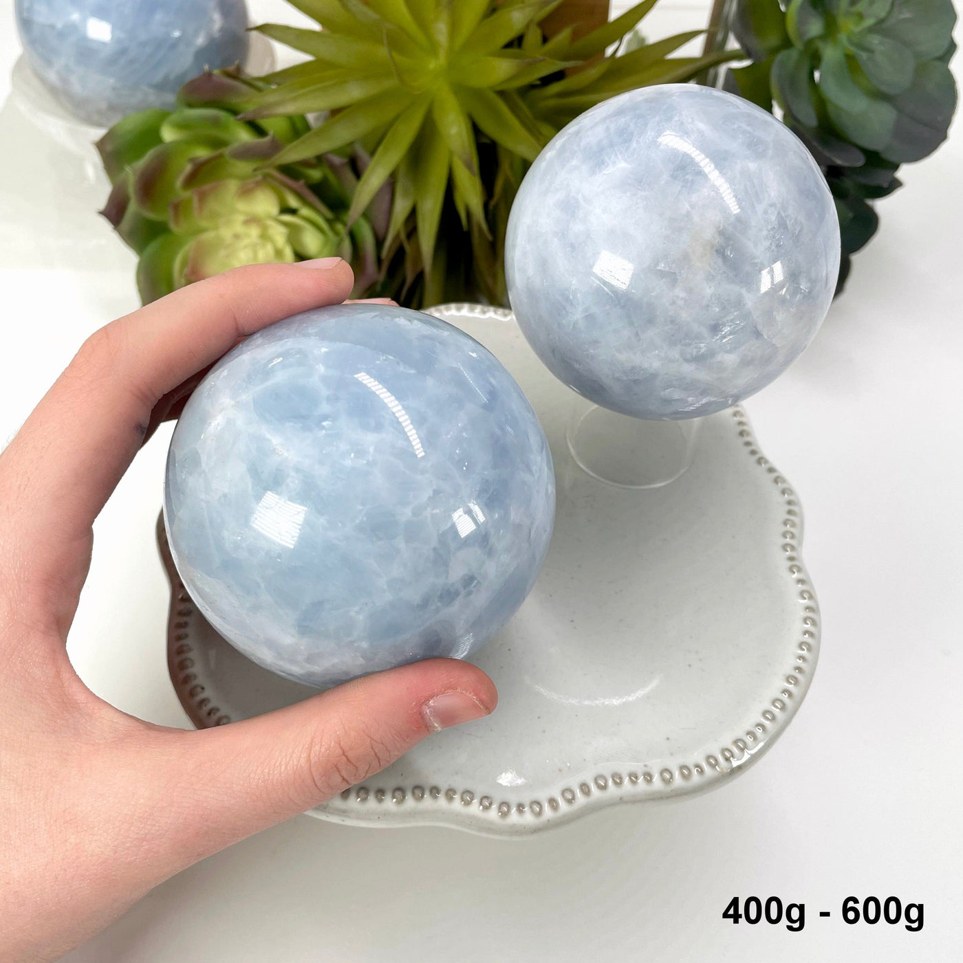 two 400g - 600g blue calcite spheres on display for possible variations with one in hand for size reference