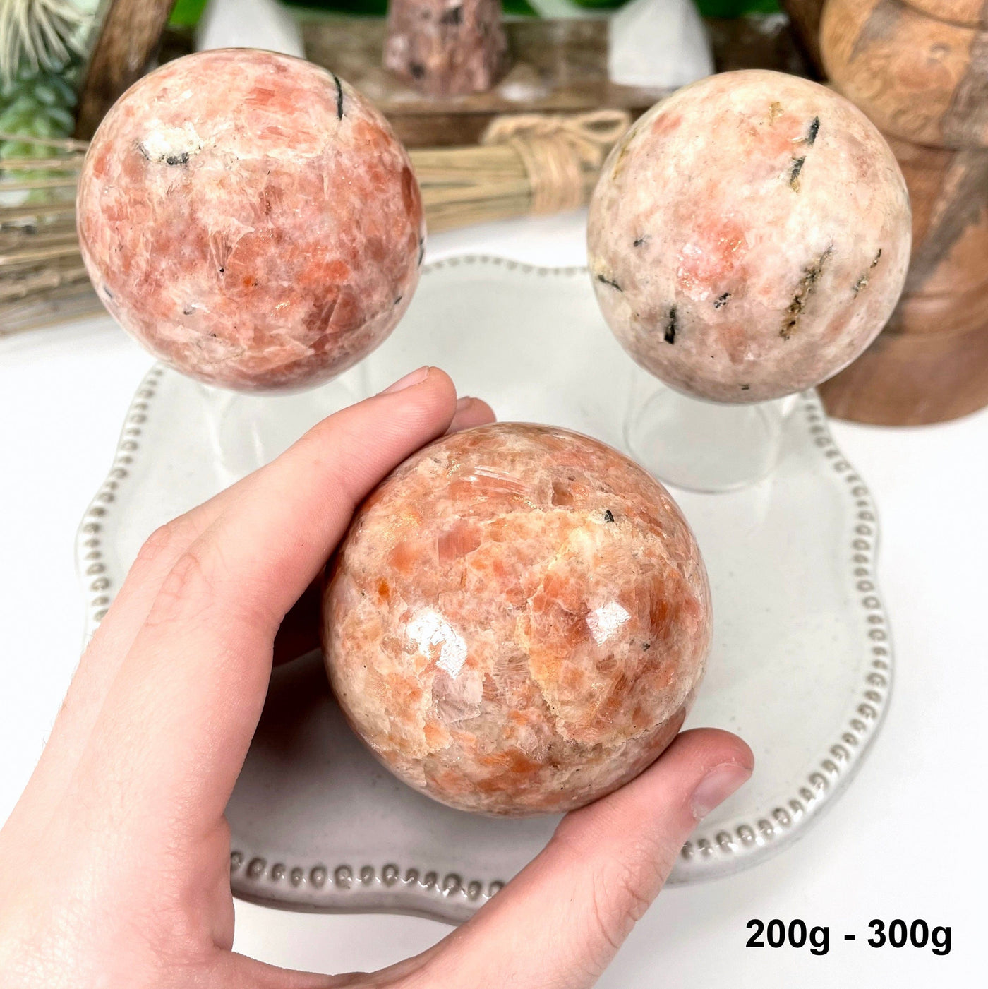 three 200g - 300g sunstone polished spheres on display for possible variations with one in hand for size reference
