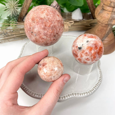 three different sunstone polished sphere weights on display for size comparison with one in hand