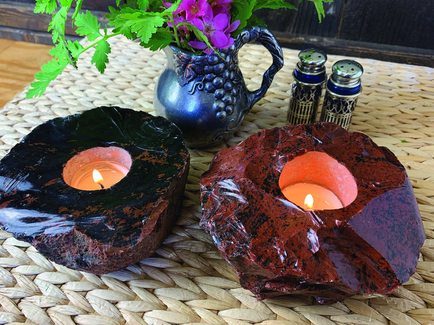 2 coffee obsidian candle holders with candles burning in both on a straw coffee table