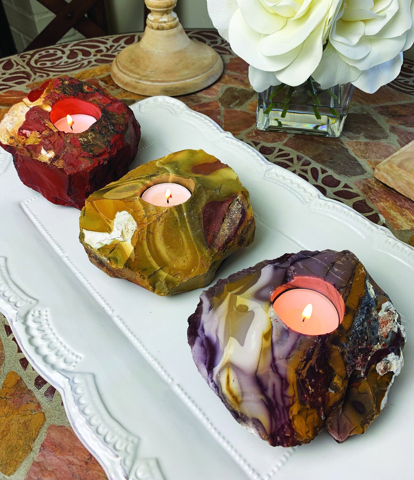 3 mookaite candle holders with candles burning in them all on a white platter