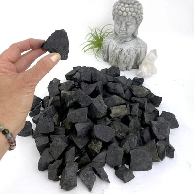 one shungite natural stone in hand for size reference with pile in backgrond