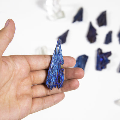 hand holding up mystic blue titanium treated kyanite blade with others blurred in the background