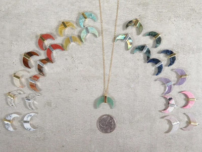 crescent pendant on gold necklace chain next to a quarter for size reference surrounded by other pendants