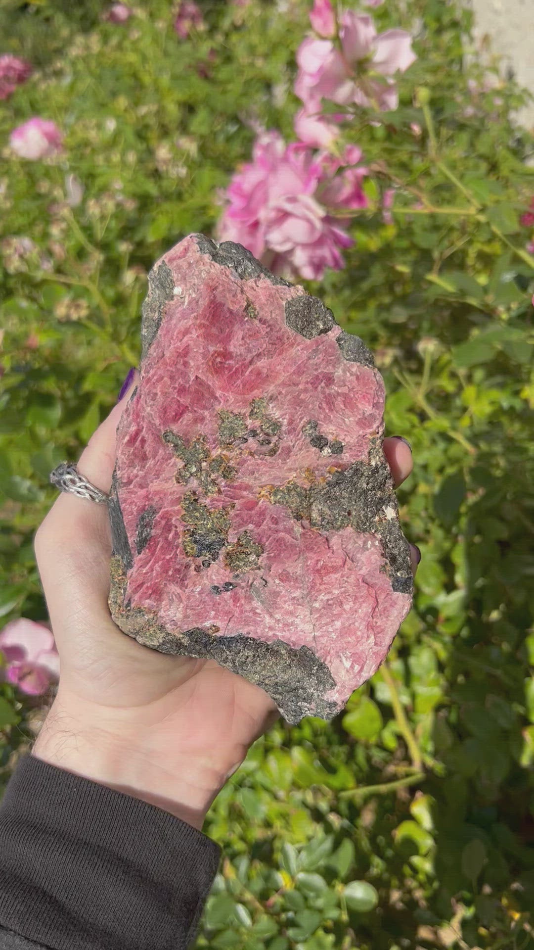 video of rhodonite stone in hand with floral background