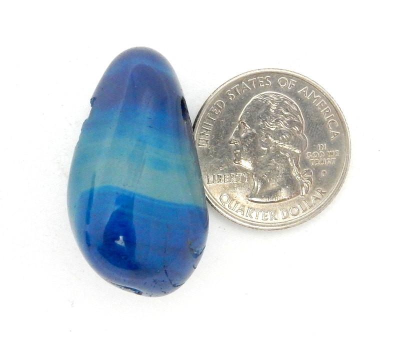 Drilled Tumbled Stone Dark Blue Agate Bead next to a quarter on White Background.