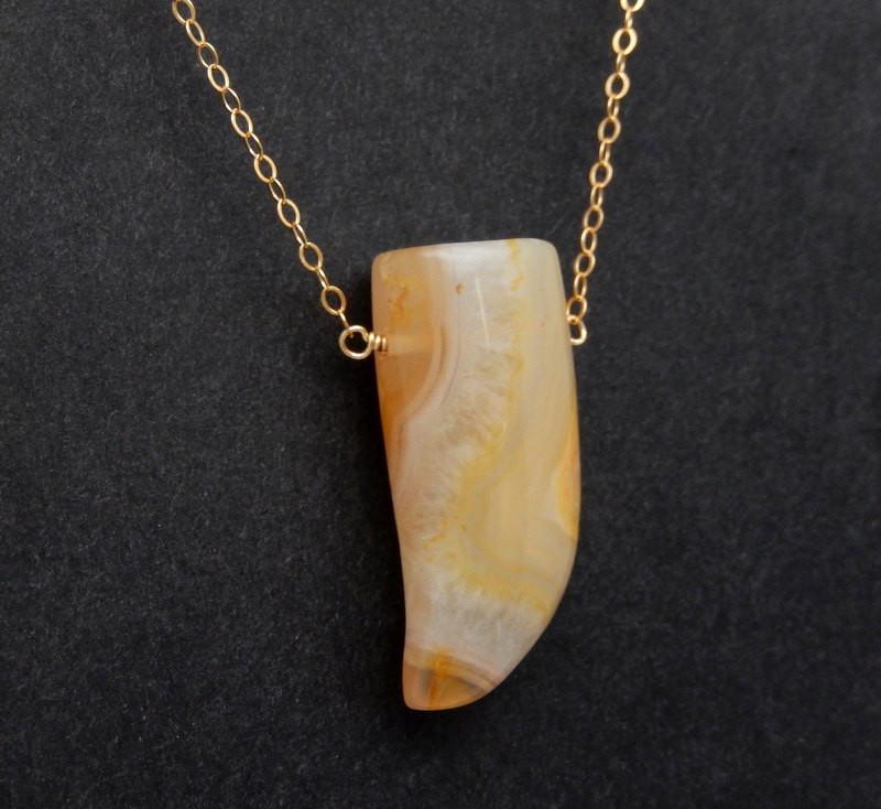 An angled close up image of an agate horn with a chain on a dark colored background.