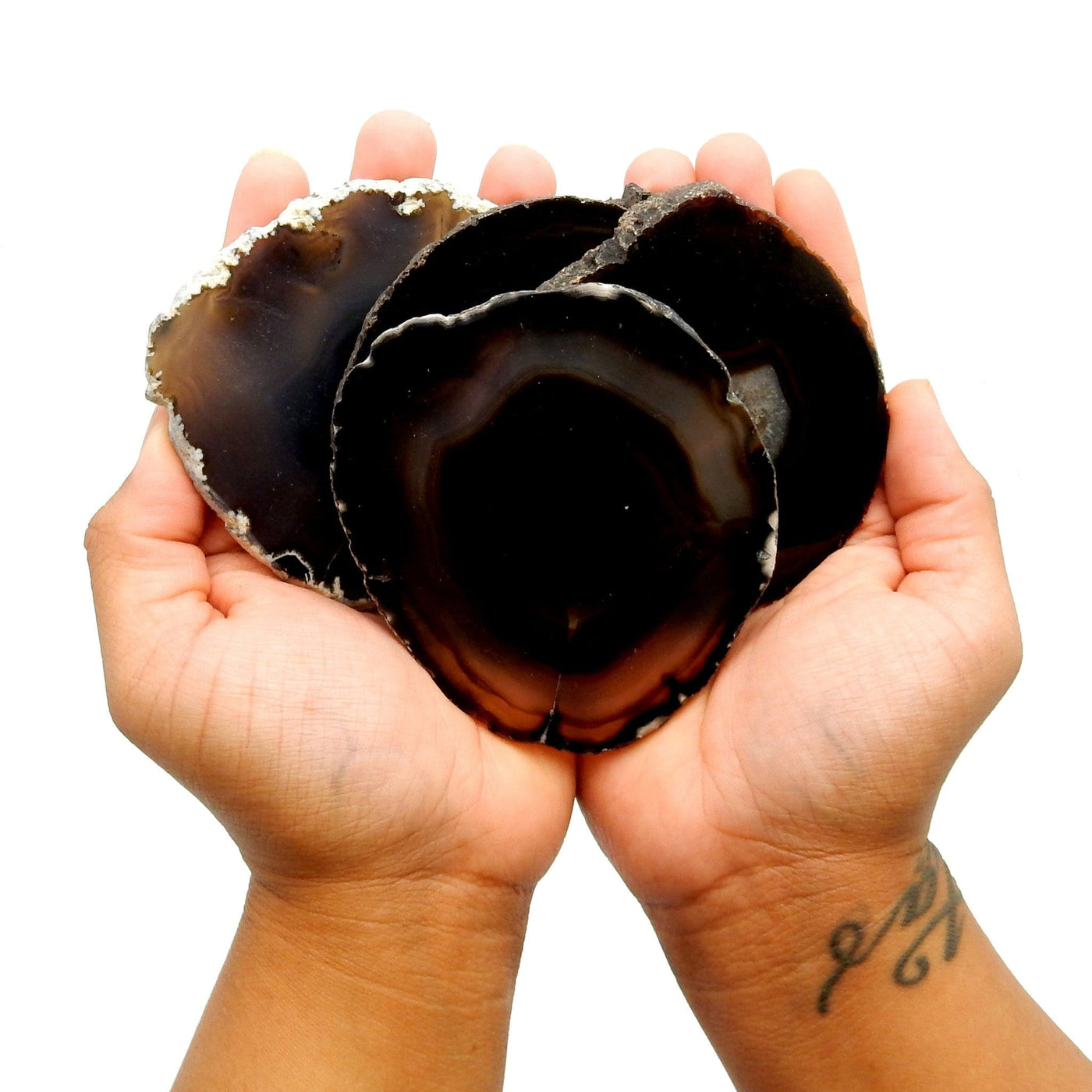 Two hands holding up 4 black agate slice coaster