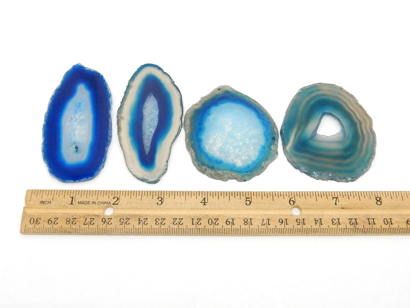 Four Blue Agate Slices lined up on a flat white surface, next to a ruler for size reference.