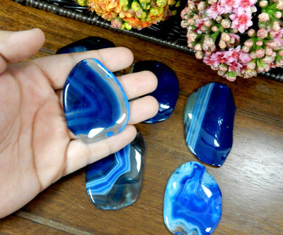 Blue Drilled Freeform Agate Slices With Polished Edge in Hand on Wooden Background.