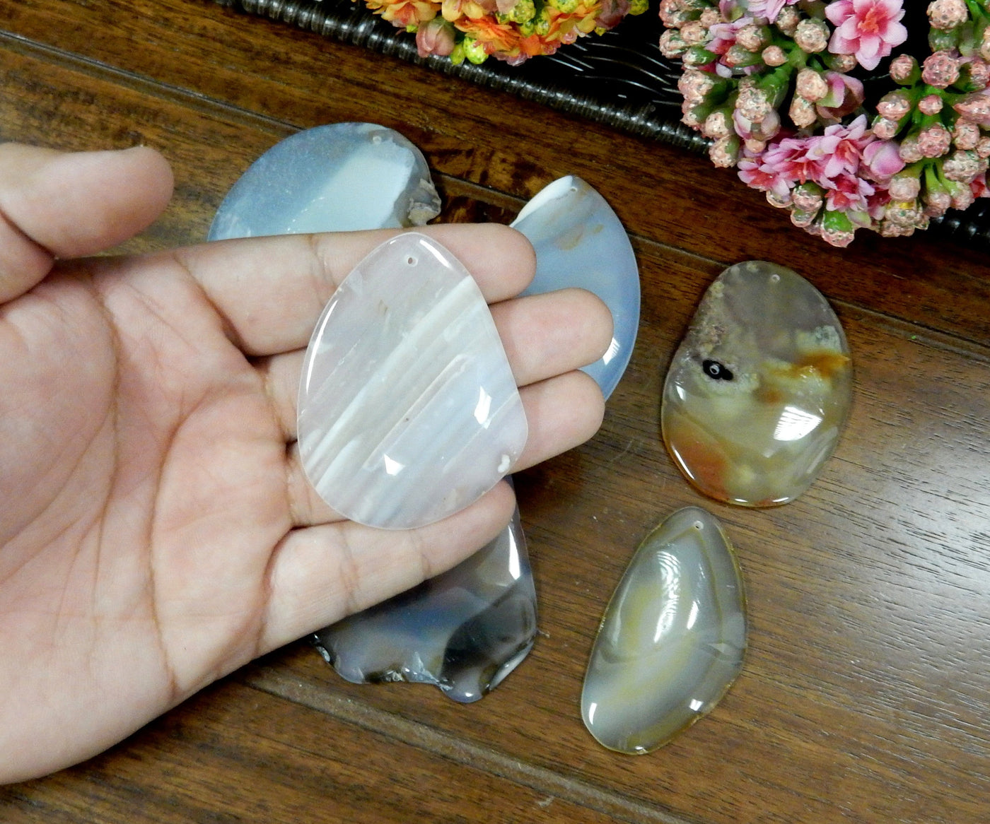 Natural Drilled Freeform Agate Slices With Polished Edge in Hand on Wooden Background.
