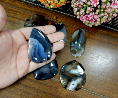 Black Drilled Freeform Agate Slices With Polished Edge in Hand on Wooden Background.